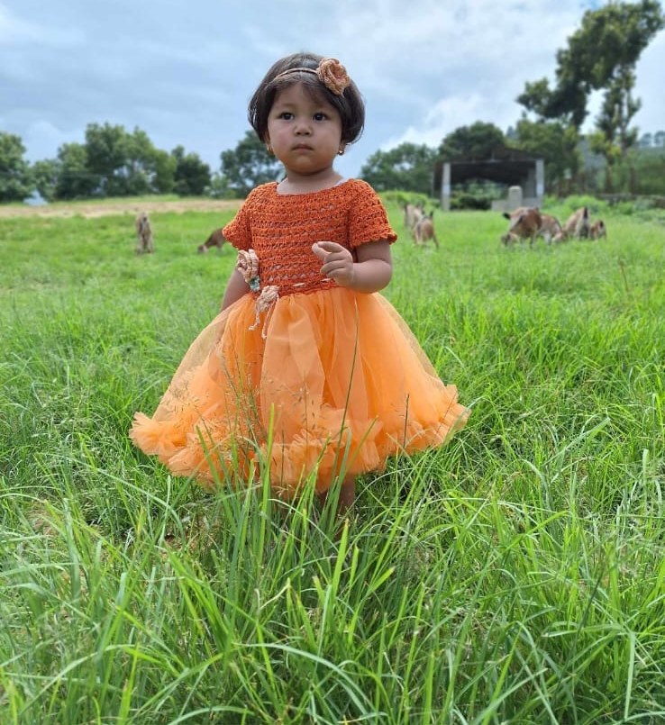 Our littlest model in an orange crochet dress, standing in a field