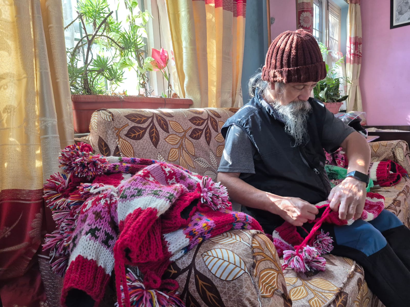 Artisan hand-knitting a pink and red woolen cap at home
